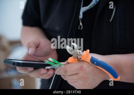 electrical engineer with wire and pliers in his hand using mobile phone while working on electrical installations in a new apartment Stock Photo
