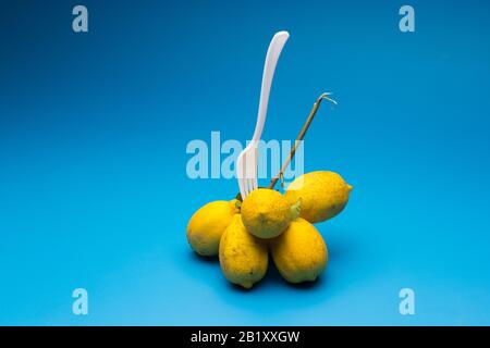 Healthy lemons with an acid flavor and full of vitamins, together with plastic cutlery; Citrus lemons on blue background. Stock Photo