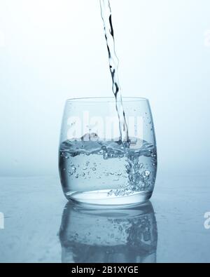Water jet falling into a glass with splashes and drops, air bubbles from a stream of water in a transparent glass. Many air bubbles in the water Stock Photo