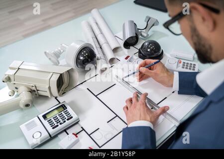 Architect Drawing Blueprint With Various Security Equipment On Desk Stock Photo