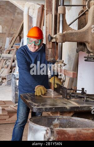 Old carpenter saws wood on a band saw in a joinery Stock Photo