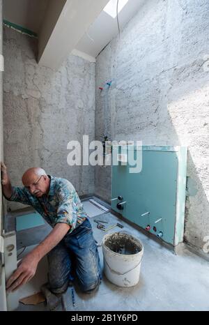 experienced senior construction worker using level tool while installing big ceramic tiles on interior concrete walls Stock Photo