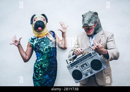 Crazy senior couple dancing for party wearing t-rex and chicken mask - Old trendy people having fun listening music with boombox stereo - Absurd and f Stock Photo