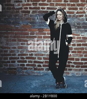 Street fashion. Young beautiful woman in fashionable cheeky modern black and white sports and casual overalls on a brick wall background Stock Photo