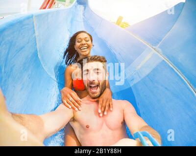 Young happy friends having fun in aqua park pipe - Cheerful multi race couple taking selfie photo with funny faces - Vacation and love concept - Soft Stock Photo