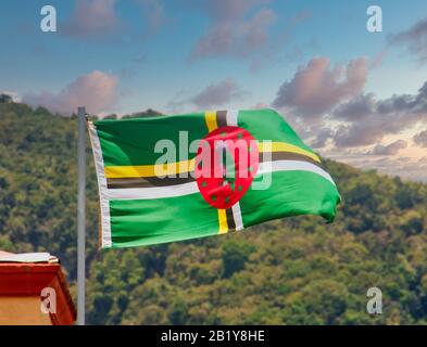 Flag of Dominica flying against tropical hills at Dsuk Stock Photo