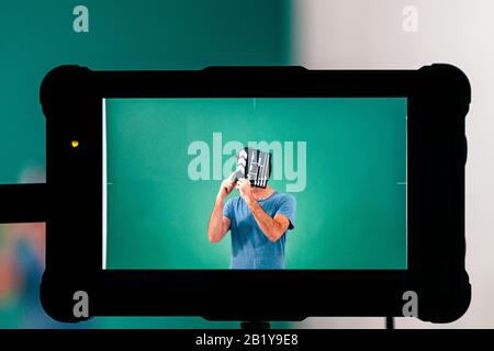 view from the screen of the movie camera of a man in studio holding a clapperboard giving action Stock Photo