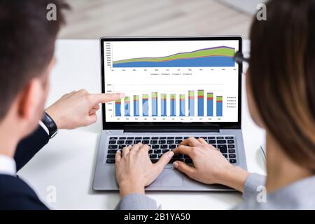 Two Businesspeople Analyzing Financial Graph On Laptop Stock Photo