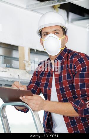 adult male builder renovating with drill in mask and helmet Stock Photo