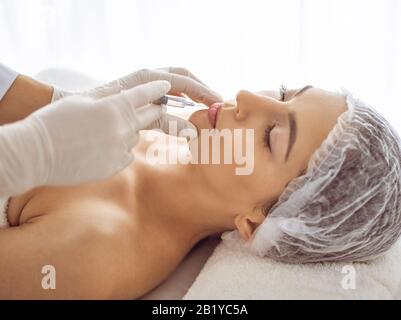 Beautician doing beauty procedure with syringe to face of young brunette woman. Cosmetic medicine and surgery, beauty injections Stock Photo