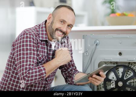 man using tablet pc to fix a washing machine Stock Photo