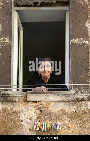 An old lady, dressed in black, looking out the window watches the people go by. Scanno, province of l'Aquila, Abruzzo, Italy Stock Photo