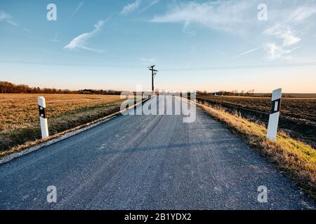 Long bending countryside road with diminishing perspective with street post along in the sunlight of the late afternoon. Seen in Franconia / Bavaria, Stock Photo