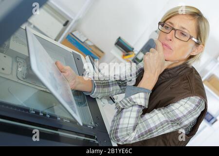 contemplative woman repairing photocopier looking at tablet Stock Photo
