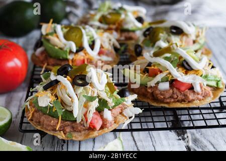 Homemade chicken tostadas with refried pinto beans, fresh cilantro, shredded cheddar cheese, avocados, black olives, sour cream, lettuce, jalapenos, l Stock Photo