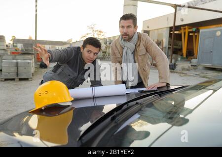 workers looking at plans spread over car bonnet Stock Photo