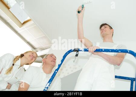 team of young workers in hardhats painting the wall Stock Photo