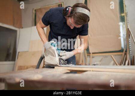Worker in safety glasses and white gloves works on jigsaw in workshop, close-up Stock Photo