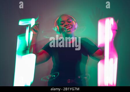African-american young woman's portrait on gradient background. Beautiful female model dancing, singing in neon lights delightful. Concept of human emotions, facial expression, sales, ad, inclusion. Stock Photo