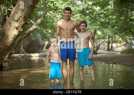 Three loving brothers standing in shallow water in a beautiful forest, family feeling love taking care