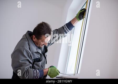 service man installing window with measure tape Man measuring window before installation of roller shutter Stock Photo