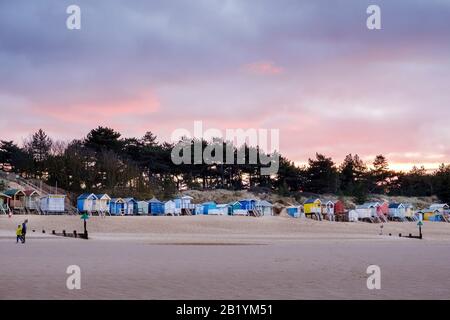 The iconic, brightly coloured beach huts on Wells beach, at sunset in winter, with the pine woods behind. Stock Photo