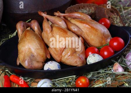 Smoked quail on a wooden background with tomatoes and eggs Stock Photo