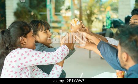 Group of Friends having fun while eating at restaurant - All friends playfully trying to steal, grab or taking food from one girls hand - teenager Stock Photo