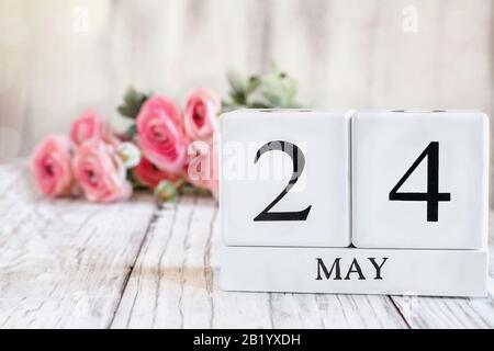 White wood calendar blocks with the date May 24. Selective focus with pink ranunculus in the background over a wooden table. Stock Photo