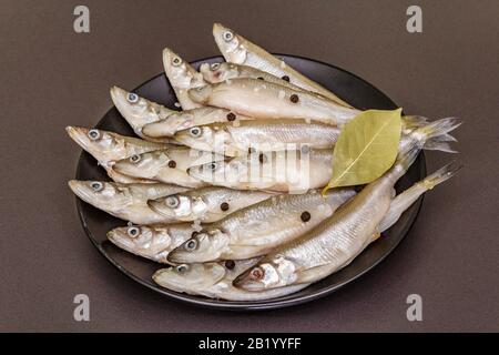 Raw sea fish smelt, sardines, anchovies, capelin with the scent of fresh cucumber ready for cooking. Healthy seafood concept. On black plate, spice. S Stock Photo