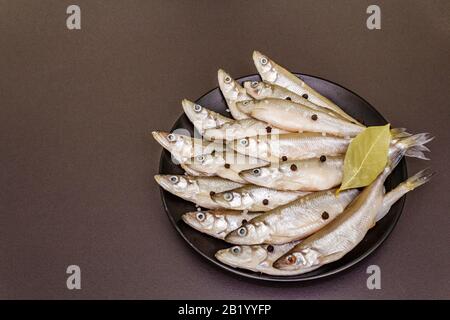 Raw sea fish smelt, sardines, anchovies, capelin with the scent of fresh cucumber ready for cooking. Healthy seafood concept. On black plate, spice. S Stock Photo