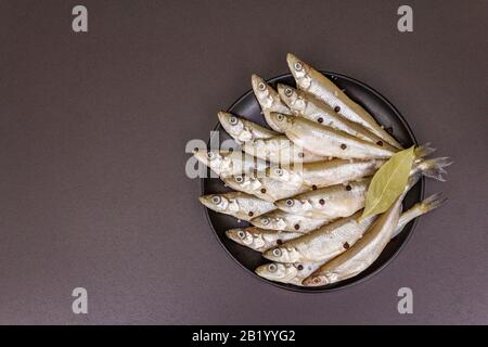 Raw sea fish smelt, sardines, anchovies, capelin with the scent of fresh cucumber ready for cooking. Healthy seafood concept. On black plate, spice. S Stock Photo