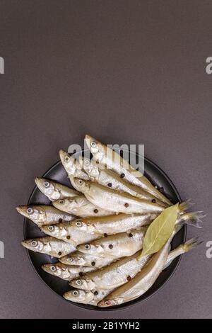 Raw sea fish smelt, sardines, anchovies, capelin with the scent of fresh cucumber ready for cooking. Healthy seafood concept. On black plate, spice. S Stock Photo