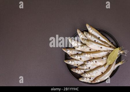Raw sea fish smelt, sardines, anchovies, capelin with the scent of fresh cucumber ready for cooking. Healthy seafood concept. On black plate, spice. S Stock Photo