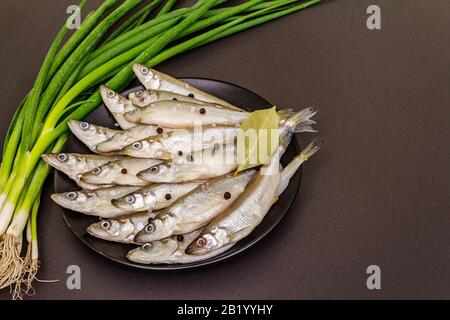 Raw sea fish smelt, sardines, anchovies, capelin with the scent of fresh cucumber ready for cooking. Healthy seafood concept. On black plate, spice, g Stock Photo