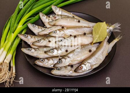 Raw sea fish smelt, sardines, anchovies, capelin with the scent of fresh cucumber ready for cooking. Healthy seafood concept. On black plate, spice, g Stock Photo
