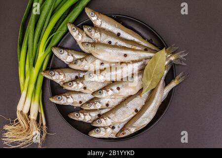 Raw sea fish smelt, sardines, anchovies, capelin with the scent of fresh cucumber ready for cooking. Healthy seafood concept. On black plate, spice, g Stock Photo