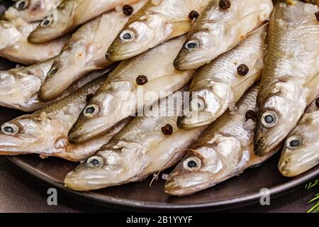 Raw sea fish smelt, sardines, anchovies, capelin with the scent of fresh cucumber ready for cooking. Healthy seafood concept. On black plate, spice. S Stock Photo