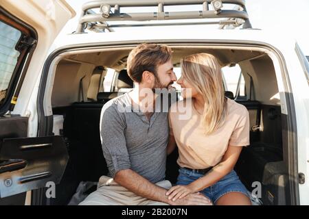 Image of a positive pleased happy young amazing loving couple outdoors hugging in car at the beach.