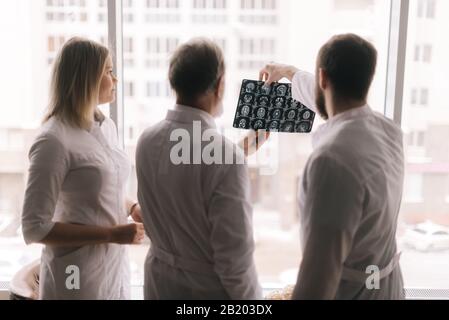 Team of three doctors discuss X-ray of patient in consulting room of hospital Stock Photo