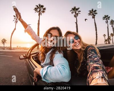 Happy young couple doing road trip in tropical city - Travel trendy people having fun driving in convertible car discovering new places