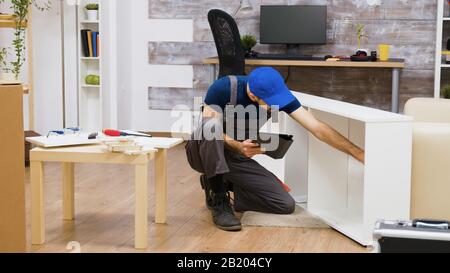Male worker using modern technology for furniture assembly in a new home. Worker with tablet computer. Stock Photo