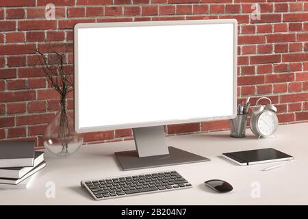 Workspace with blank computer monitor white screen mock up on the white desk near red brick wall Stock Photo