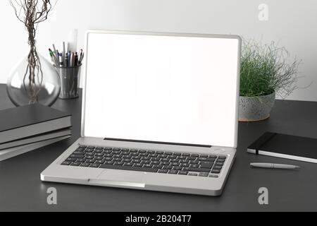 Workspace with blank laptop monitor white screen mock up on the black desk near white wall Stock Photo