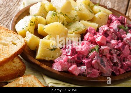 herring salad with beets, onions, apples, pickled with a side dish of boiled potatoes close-up in a plate on the table. horizontal Stock Photo