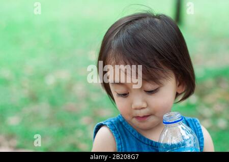 Asian toddler girl drinking water from the plastic water bottle. Stock Photo