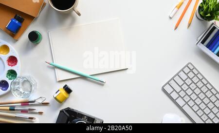 Top view image of Graphic designer working table flat lay with painting/drawing equipment, color, paintbrush, pencils, white blank paper, coffee cup, Stock Photo