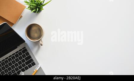 Top view image of white working desk with accessories putting on it. Flat lay Computer laptop, Coffee cup, Potted plant, Notebook. Modern and Orderly Stock Photo