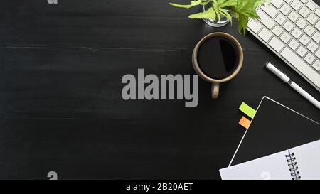 Top view image of black wooden table with accessories putting on it. Flat lay White keyboard, Coffee cup, Potted plant, Notebook. Modern and Orderly s Stock Photo