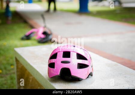 Pink helmet on the concrete bench in the park with pink push bike in the background. Stock Photo
